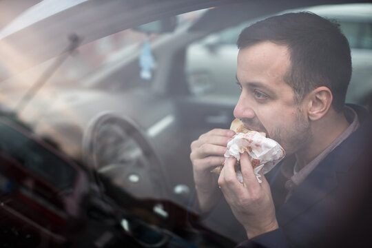Handsome young man eating a hurried lunch in his car (color toned image; shallow DOF)