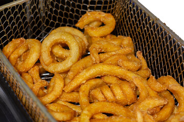 Curly fries, coated in herbs and spices, cooking in a deep fat fryer basket.  Fast food concept