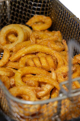Curly fries, coated in herbs and spices, cooking in a deep fat fryer basket.  Fast food concept
