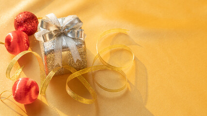 Silver gift box, gold ribbon, and red Christmas ball on a gold background.