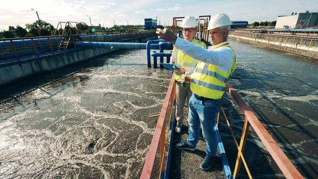 Wastewater operators taking a water sample at a sewage cleaning reservoir