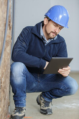 tradesman crouching and looking at a tablet