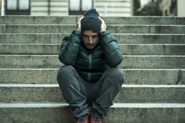 dark and edgy urban portrait of middle aged sad and depressed unemployed man sitting outdoors on dirty street corner staircase feeling upset suffering depression problem