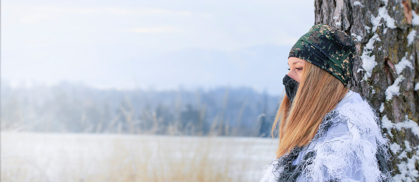 Portrait a young beutiful hunter woman , she is  wearing winter camouflage . In the background are snowy trees. Banner photo.