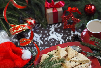 A cup of hot coffee with homemade shortbread cookies and red Christmas decor on a knitted knitted background with deer. Congratulatory background. Christmas background.