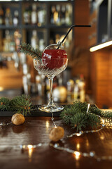 Tasty red cocktail in glass in shape of Christmas toy bauble garnished with spruce branch and placed on wooden counter in bar for winter holidays party 