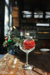 Fresh red alcohol cocktail in glass in shape of Christmas ball placed on wooden table in bar for New Year party celebration 