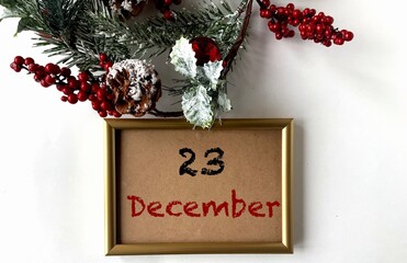 December 23 on craft paper in a gold frame.Nearby fir branches, cones and red berries on a white background.The first month of winter.Calendar for December.