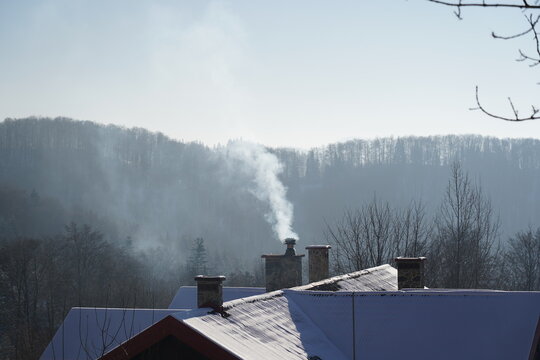 White smoke from the chimney of mountain hut in winter sunny cold day