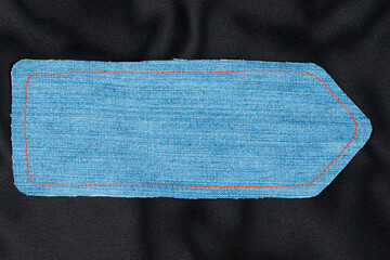 Denim arrow with orange threads lies on black silk.