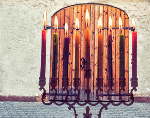 Digitally composite image with menorah and burning candles and old wooden door in old European city, concept of holidays in December 2020