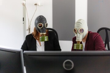 Man and woman working on a computer in the office, businesspeople in a suit with gas mask against...