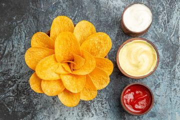 Overhead view of homemade potato chips decorated like flower shaped and salt with ketchup mayonnaise on gray background