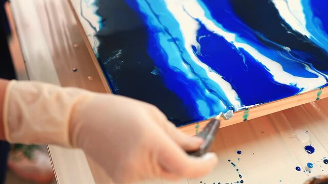 Close-up of making a line on paint in a painting. A gloved hand holds a spatula and guides over the paint. The mental process of the free realisation of thought and the uniqueness of the work.
