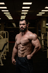 Obraz na płótnie Canvas strong young bearded caucasian man with perfect sport physique body in dark fitness bodybuilding gym