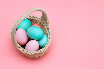 Easter decor: colored eggs in a basket, pink background. Preparing for Easter. The photo