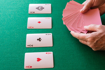 Top view of woman's hands, with poker cards and aces, on green playing mat, horizontal