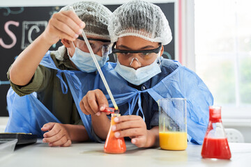 Attentive children in protective masks and gowns mixing reagents