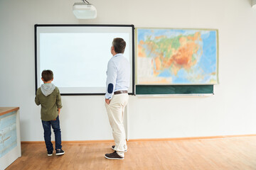 Little dark-haired boy standing near the interactive whiteboard