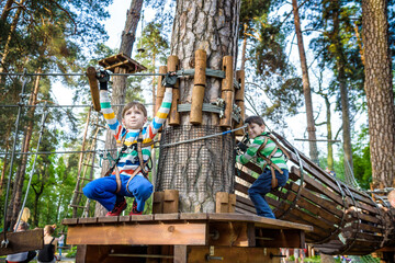 Two little boy boys kid in a helmet and with a safety carbine goes on a rope on the background of...
