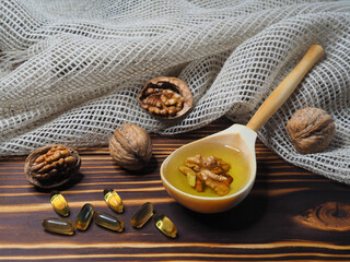Juglans regia fruit, walnut oil in capsules and a wooden spoon on a wooden background with a...