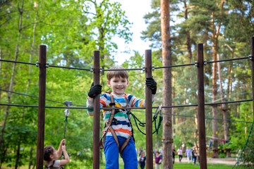 Cute boy enjoying a sunny day in a climbing adventure activity park. shadows from a rope