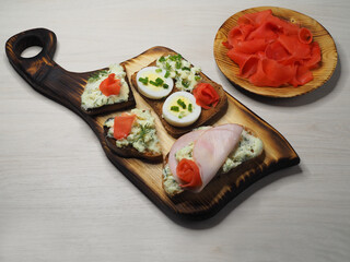 Sandwiches, bruschetta, cheese toast, ham, spicy herbs, egg and pickled ginger on a wooden Board, light background, top view. Fast food recipe, snack with fried bread for a holiday and picnic
