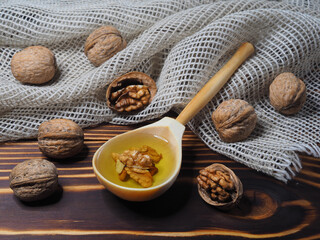 Juglans regia fruit and walnut oil in a wooden spoon on a wooden background with a napkin, closeup. Healthy delicacy oil and walnut kernels with vitamins, antioxidants and omega for proper nutrition