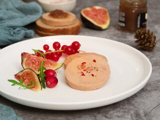 A sliced pieces of traditional French foie gras on a white plate with fig fruit,red currant, rocket vegetable. Pot of onion marmalade in background. It's popular, well-known delicacy in French cuisine © Pkheawtasang