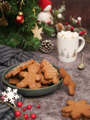 Fototapeta na wymiar A plate of various Christmas sugar cookies decorated with royal icing and a cup of hot chocolate in and xmas tree in background. With cozy atmosphere holidays greetings festive