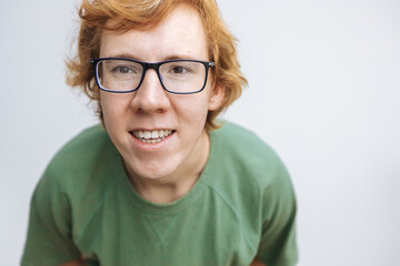 red-haired man in glasses and a green T-shirt looks at the camera and smiles on a white background