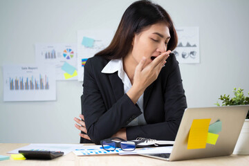 Young pretty business lady lawyer is yawning at her work place with cup of coffee in the hand, in smart outfit, with glasses