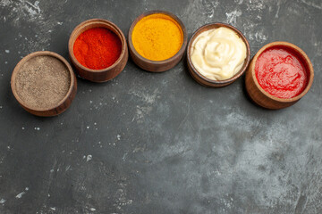 Above view of set for sauces containing different spices mayonnaise and ketchup on gray background