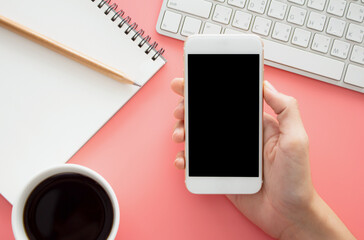 Mockup image of hands holding white mobile phone with blank white .screen with  Modern pink office desk 