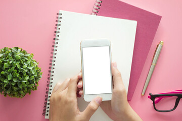 Mockup image of hands holding white mobile phone with blank white .screen with  Modern pink office desk with laptop and other supplies for input the text on copy space Top view, flat lay.