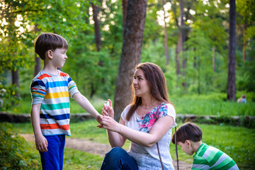 Young woman mother applying insect repellent to her two son before forest hike beautiful summer day or evening. Protecting children from biting insects at summer. Active leisure with kids