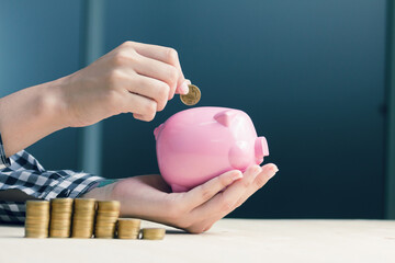 closeup women hand putting coin into a piggy bank  in finance banking and saving concept