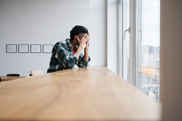 Fototapeta premium Sad young man in a medical mask sitting near the window
