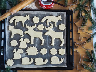 The process of making animal shaped Christmas cookies and cookie cutters on a black baking sheet from the kitchen oven among spruce branches. Festive pastry christmas background. Home cooking.