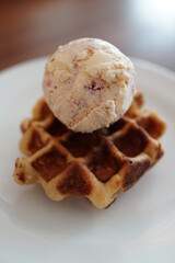 A scoop of strawberry flavor ice cream on a plain waffle