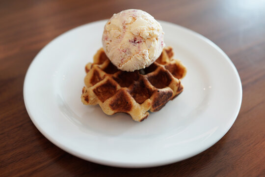 A scoop of strawberry flavor ice cream on a plain waffle