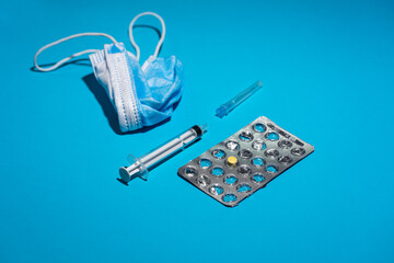 Blue face mask, pills, syringe on blue background. Medicine and healthcare. Medications and pharmacy.