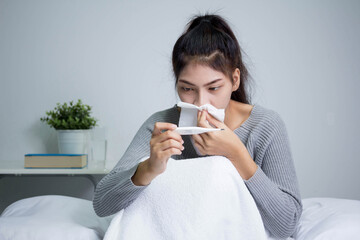 Young sick girl with fever checking her temperature with a thermometer at home