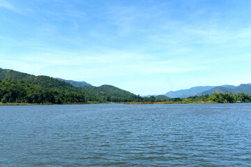 Landscape of the mountains and river near the dam, focus on the natural summer day light blue sky with clouds in the background