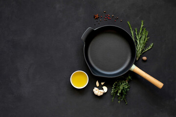 Cast iron frying pan with vegetables, spices and herbs on a black background.