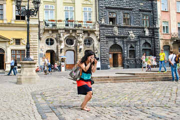 Fototapeta na wymiar Young woman photographing on city street in Lviv, Ukraine. Girl looking in camera and takes pictures in downtown