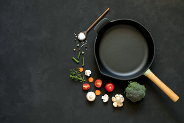 Fototapeta na wymiar Cast iron frying pan with vegetables, spices and herbs on a black background.
