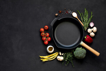 Cast iron frying pan with vegetables, spices and herbs on a black background.