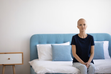 Portrait of young woman oncology patient at modern ward in cancer treatment clinic. Millennial hairless female get medical therapy at oncological center sit on hospital bed look at camera. Copy space