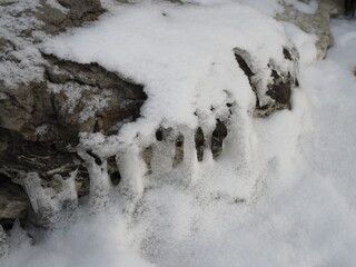 Ice and icicles of different shapes above the water in the river. Clear water in the river. Sunny day. Icicles close up.